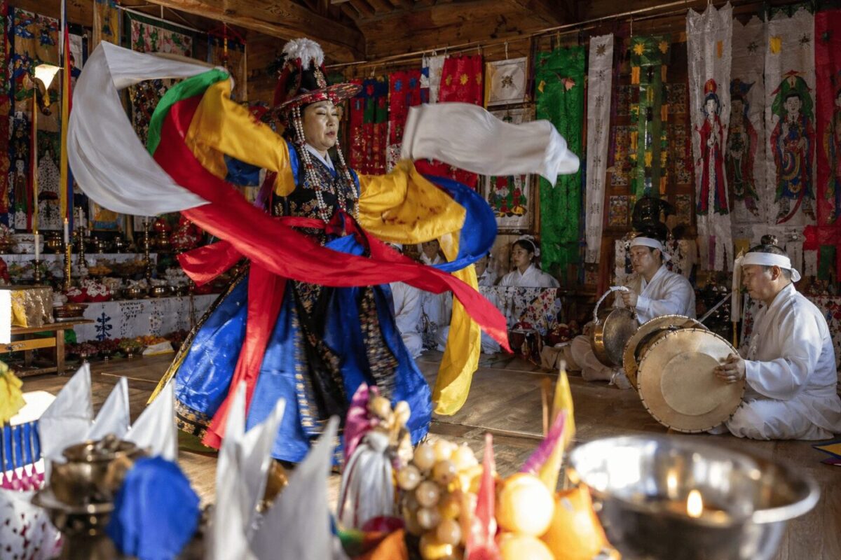 Mudang performing a traditional Korean gut ritual dance with janggu and jing musicians in a shrine