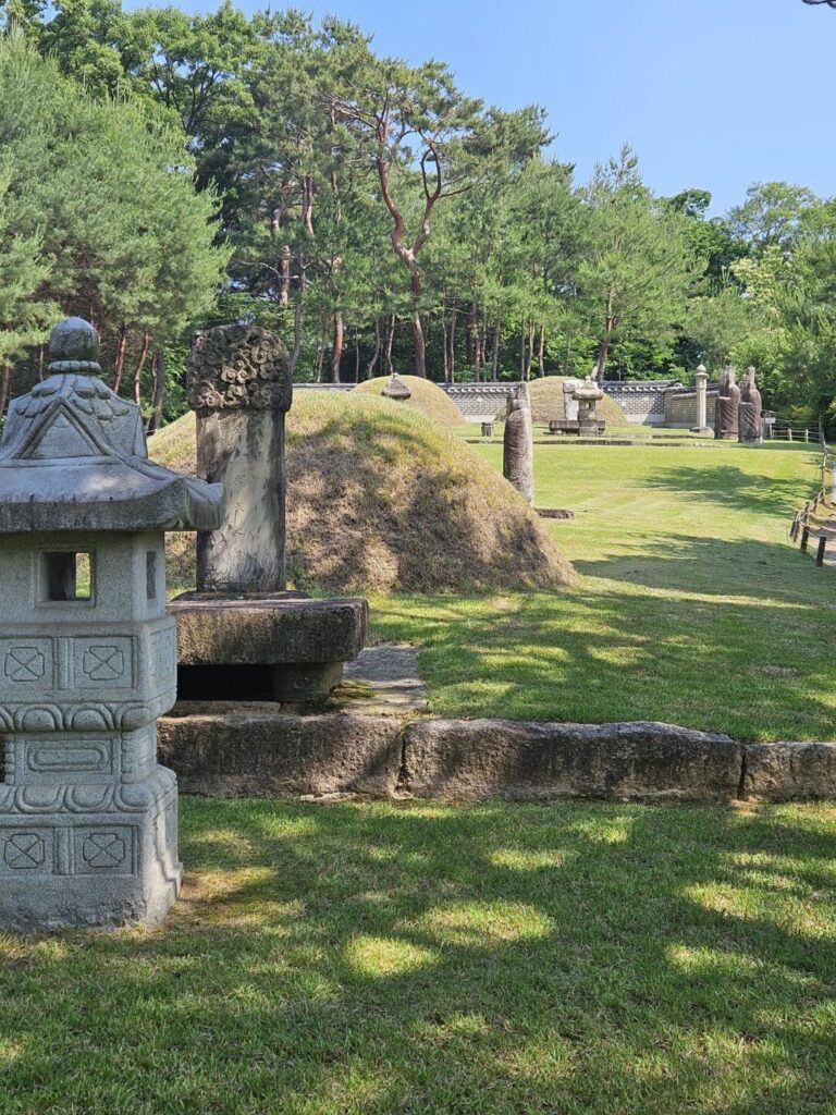 A stone lantern in the foreground with the tomb mounds and pine trees of Yeonsan-gun's tomb complex in the background
